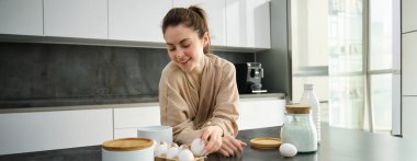 Çekici, genç, neşeli kız mutfakta yemek pişiriyor, para kazanıyor, yemek tarifi kitabını tutuyor, fikirleri var..