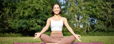 Sportif kadın temiz hava üzerine meditasyon yapıyor, spor minderinde oturuyor ve yoga yapıyor, mutlu bir şekilde gülümsüyor. Spor ve insanlar konsepti.
