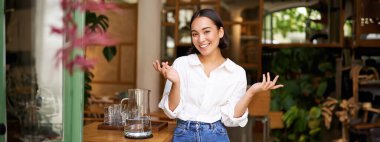 Beyaz yakalı, gülümseyen Asyalı bir kızın portresi, kafede çalışıyor, restoran işletiyor, kendine güvenen ve şık görünüyor..
