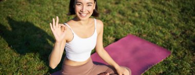 Asyalı bir kadının portresi lastik mindere oturmuş, meditasyon yapıyor, işaret veriyor ve kameraya bakıyor, yoga yapıyor..