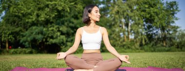 Sportif kadın temiz hava üzerine meditasyon yapıyor, spor minderinde oturuyor ve yoga yapıyor, mutlu bir şekilde gülümsüyor. Spor ve insanlar konsepti.