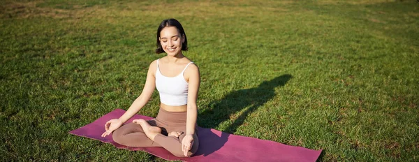 Özenli genç bir kadının portresi, yoga, egzersiz, nefes alıp verme, parkta temiz hava, lastik paspasın üzerinde oturmak..