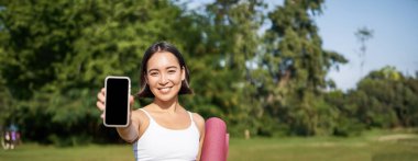 Zinde ve sağlıklı Asyalı bir kadının dikey çekimi. Antrenman istatistikleriyle akıllı telefon ekranı gösteriyor. Telefon uygulaması öneriyor..