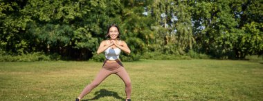 Refah ve spor kompleksi. Genç Asyalı kadın esniyor, çömeliyor ve temiz hava alıyor, gülümsüyor..