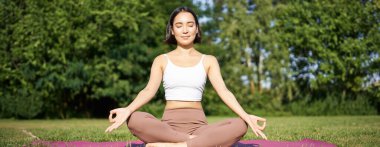 Sportif kadın temiz hava üzerine meditasyon yapıyor, spor minderinde oturuyor ve yoga yapıyor, mutlu bir şekilde gülümsüyor. Spor ve insanlar konsepti.