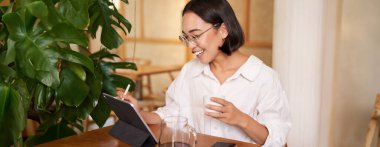 Genç ressam dijital tablet çiziyor, grafik kalem kullanıyor, kafede kahve içiyor ve smth saçıyor..