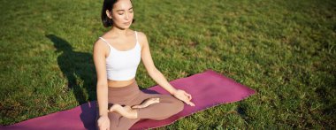 Gülümseyen Asyalı kadının portresi meditasyon yapıyor, temiz havada yoga yapıyor, lastik minderde dinleniyor, parkta egzersiz yapıyor, hava soluyor, sakin oluyor..