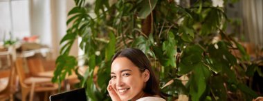 Kafede oturan, kameraya gülümseyen, kahve içen, dizüstü bilgisayar kullanan, uzaktan çalışan, interneti araştıran,.