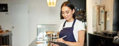 Gülümseyen tatlı barista kız, kafede çalışan Koreli kadın, düzeni sağlamak için tablet kullanıyor, tezgahta kahve yapıyor..