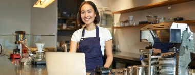 Genç bir kafe sahibinin portresi, dizüstü bilgisayarına bakmak, sipariş almak, kahve dükkanında müşteriye hizmet etmek..