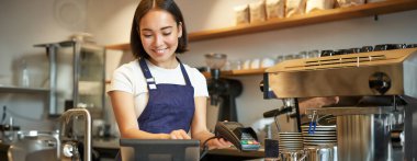 Gülümseyen Asyalı barista kız işlem sırası, POS terminaline girin, kahve dükkanında tezgahta çalışın..