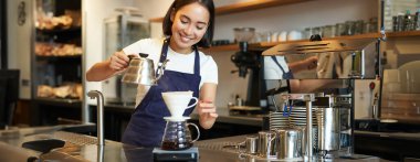 Şirin esmer kız barista, çaydanlıktan su dolduran kafe personeli ve tezgahın arkasında filtre kahve hazırlayan, sipariş hazırlayan.