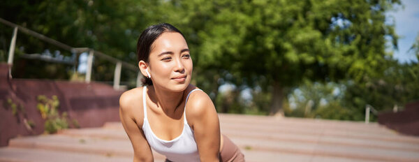Portrait of asian woman taking break, breathing heavily and panting after running, jogger standing and wiping sweat off forehead, smiling pleased.
