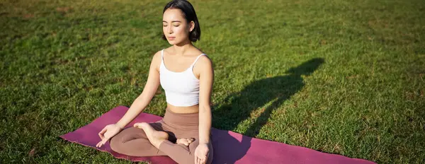 Farkındalık ve meditasyon. Genç Asyalı kadın yoga yaparken gülümsüyor, Asana 'da lastik minder üzerinde dinleniyor, parkta temiz hava egzersizleri yapıyor..