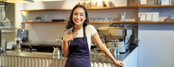 Portrait of smiling asian entrepreneur, independent coffee shop owner, wearing apron, working in cafe, wearing apron.