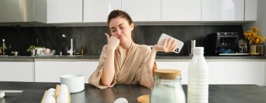 Çekici, genç, neşeli kız mutfakta yemek pişiriyor, para kazanıyor, yemek tarifi kitabını tutuyor, fikirleri var..