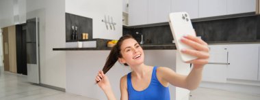 Genç sporcu kadının yakın portresi, fitness kızı egzersiz yaparken selfie çekiyor, yoga minderinde poz veriyor, akıllı telefonu tutuyor ve gülümsüyor..