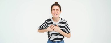 Mutlu, gülümseyen genç bir kadının portresi gözleri kapalı durur, ellerini kalbe tutar, güler, komik bir şey hatırlar, beyaz arka planda izole edilmiş..