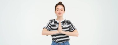 Düşünceli genç bir kadının portresi meditasyon yaparken, el ele tutuşurken, namaste hareketi yaparken, yoga yaparken, beyaz arka planda dururken..