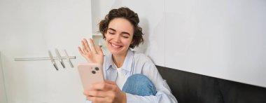 Mutlu gülümseyen kız, görüntülü konuşmada arkadaşına merhaba diyor, akıllı telefon uygulamasına el sallıyor, telefonundaki çevrimiçi sohbete bağlanıyor..