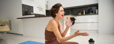 Kaygısız fitness kızı, antrenman eğitmeni evde su şişesiyle oturur, yoga minderi giyer, eşofman giyer, akıllı telefonuna şarkı söyler, kablosuz kulaklıkla müzik dinler, pilates yoga sırasında şarkı dinler..