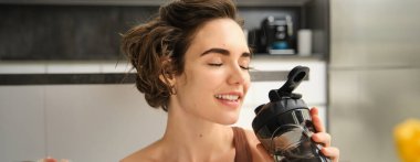 Güzel sporcu kadının yakın portresi. Kız sporcu şişeden su içiyor. Genç fitness kadını, antrenmandan sonra susamış, evde egzersiz yapıyor..