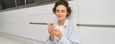 Akıllı telefonlu mutlu bir kızın kapalı çekimleri, evde oturup cep telefonu kullanması, uygulamadan video izlemesi, uygulamadan arkadaşlarıyla sohbet etmesi..
