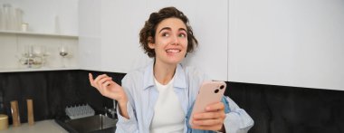 Mutfakta hevesli bir kız, akıllı telefonu tutuyor heyecanlı görünüyor, gülümsüyor ve dudağını ısırıyor, müstehcen konuşmayı deniyor, cep telefonuyla konuşuyor..