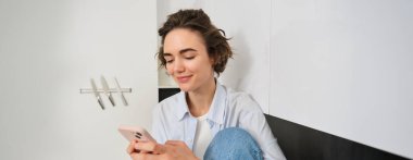 Evde cep telefonuyla oturan bir kadının portresi, akıllı telefon uygulaması üzerinden online alışveriş, içeride zaman geçirmek..