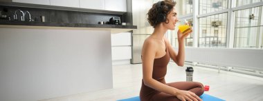 Spor ve sağlıklı yaşam tarzı. Sporcu kadın evde, spor yapıyor, spor yaptıktan sonra portakal suyu içiyor, lastik paspasla spor yapıyor..