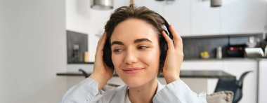 Mutlu, gülümseyen bir kızın yakın portresi, kablosuz kulaklık takar, müzik dinler ya da e-kitap dinler, evde koltukta oturur. Boşluğu kopyala