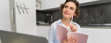 Genç iş kadınının portresi, evden çalışıyor, planlama yaparken düşünceli görünüyor, online dersler sırasında notlar alıyor, Webinar 'dan bilgi alıyor..