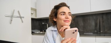 Evde güzel bir kadının portresi, elinde akıllı telefon, cep telefonu uygulamasından online alışveriş..