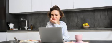 Genç bayan girişimci evlerden çalışır. Bilgisayarlı kız mutfağında oturuyor, ev ödevlerini yapıyor, uzaktan kumandayla çalışıyor, online toplantılara bağlanıyor, notlar alıyor..