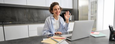 Mutlu genç kadın, öğretmenlik öğrencileri online. Kız uzaktan iş toplantısına ev bilgisayarından bağlanıyor, merhaba diyor, bilgisayara el sallıyor..