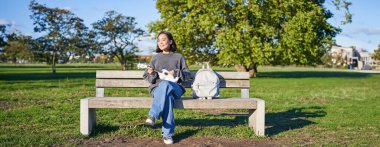 Kaygısız kız parktaki bankta ukulele ile oturur, güneşli bir günde açık havada çalar ve şarkı söyler..