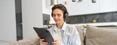 Mutlu bir kadının portresi, kulaklıkla tabletten video izlerken, dijital cihazını kullanarak evde çalışırken, e-kitap okurken müzik dinlerken..