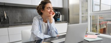 Çalışan kadın evde dizüstü bilgisayar kullanıyor, vergi işlemlerini yapıyor, mutfakta online ders izliyor..