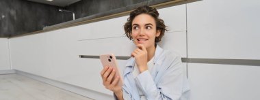 Gülümseyen bir kadın görüntüsü, akıllı telefon kullanmak ve düşünmek, karar vermek, cep telefonundan online alışveriş.