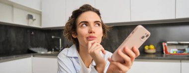 Evde güzel bir kadının portresi, elinde akıllı telefon, cep telefonu uygulamasından online alışveriş..