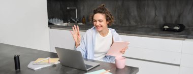 Gülümseyen genç bir kadının portresi selam söylüyor, dizüstü bilgisayara el sallıyor, hocasıyla görüntülü konuşmalar yapıyor. Öğretmen çevrimiçi bir derse bilgisayarla bağlanıyor, evde mutfakta çalışıyor..