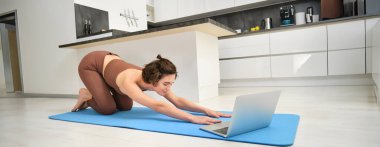 Kız sporcu imajı, sporcu kadın yogası, online video dersini laptopta takip etmek, bilgisayardaki antrenman talimatlarını izlemek, evden egzersiz yapmak..