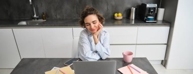 Çalışan genç bir kadının görüntüsü, dizüstü bilgisayara bakıyor, evde oturuyor ve Webinar izliyor, takım toplantısına bağlanıyor, kapalı alanda ders çalışıyor..