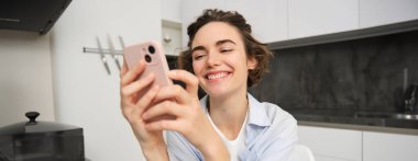 Cep telefonundaki esmer kadın sohbetlerinin portresi, evden akıllı telefon uygulaması, mutfakta otururken siparişler..