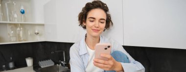 Cep telefonunu kontrol eden, akıllı telefondan mesaj okuyan ve gülümseyen genç bir kadının portresi..