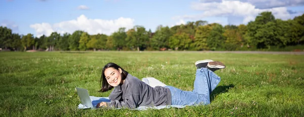 Leisure and people. Happy young woman lying in park on blanket, using laptop, relaxing outdoors and watching videos online on computer.