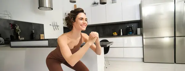 stock image Image of young woman doing squats at home, workout on rubber mat in bright room indoors, wearing activewear for training. Copy space