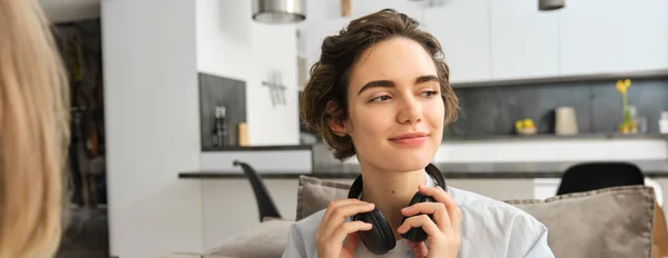 Close up portrait of young woman with short hair, takes of her headphones, finishes listening to ebook, spends time alone at home with music.