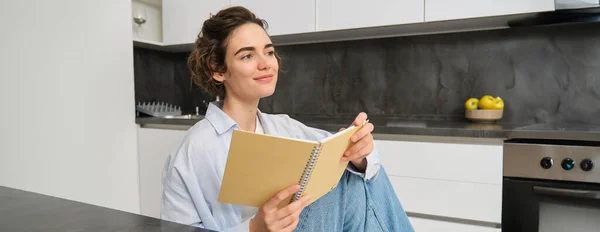 stock image Portrait of young adult woman, reading her notes, holding notebook and smiling, relaxing at home.