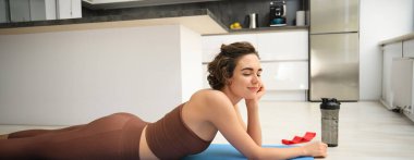 Spor ve sağlıklı yaşam tarzı. Esmer sporcunun portresi aktif giyimde spor yapıyor, yerde kauçuk mindere uzanıyor, mutfakta egzersiz yapıyor, spor şişesinden su içiyor..